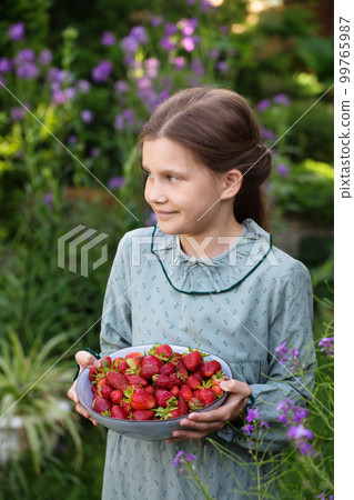 Cute girl in a vintage dress with a bowl of ripe strawberries in the garden Cute girl in a vintage dress with a bowl of ripe strawberries in the garden 99765987
