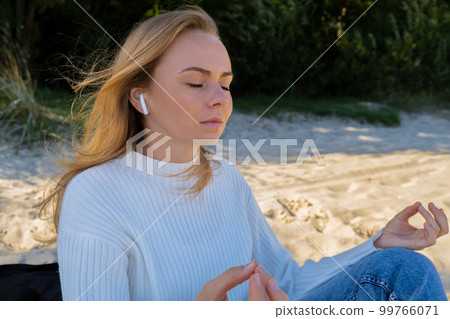 Happy young woman on the beach sea ocean. Wearing wireless headphones doing audio healing sound therapy being mindful Leisure in nature. Wellbeing unity with nature health mindfulness Happy young woman on the beach sea ocean. Wearing wireless headphones doing audio healing sound therapy being mindful Leisure in nature. Wellbeing unity with nature health mindfulness 99766071