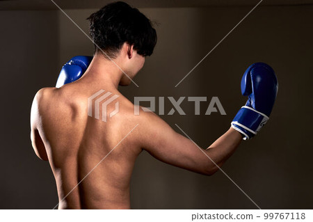 Rear view of a young man wearing boxing gloves Rear view of a young man wearing boxing gloves 99767118