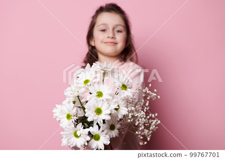 Adorable 5 years old child, lovely little girl in pink pastel clothes, smiling and holding out at camera a cute bouquet of white flowers, isolated background. Flowers as a cute present for any event 99767701