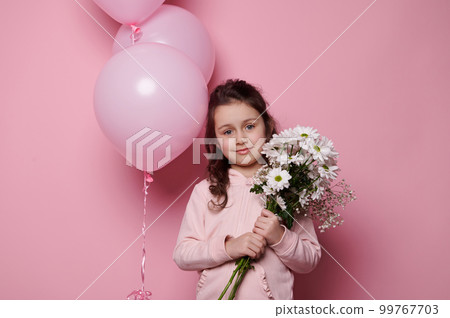 Little girl holding bouquet of white chrysanthemums and gypsophila flowers, smiling at camera, isolated on pink background with pink pastel helium balloons. International Children's Day. Mother's Day 99767703