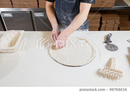 Dough for pizza, the chef rolls out the blanks. Closeup hand of chef baker in uniform white apron cook pizza at kitchen Dough for pizza, the chef rolls out the blanks. Closeup hand of chef baker in uniform white apron cook pizza at kitchen 99768016