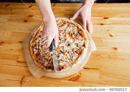Closeup hand of chef baker in uniform blue apron cutting pizza at kitchen 99768017