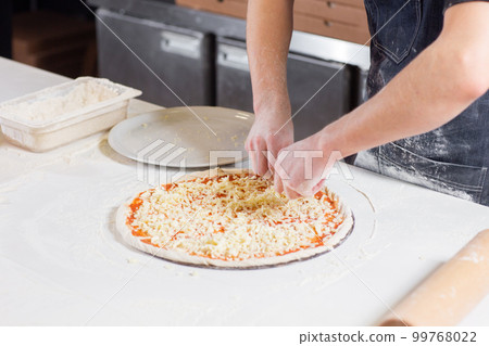 Cooking pizza. arranges cheese ingredients on the dough preform. Closeup hand of chef baker in uniform white apron cook at kitchen 99768022