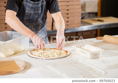 Cooking pizza. arranges cheese ingredients on the dough preform. Closeup hand of chef baker in uniform white apron cook at kitchen 99768023