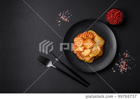 Delicious crispy fried potatoes in slices on a black ceramic plate 99768737