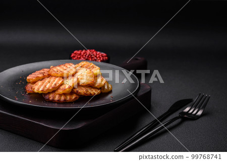 Delicious crispy fried potatoes in slices on a black ceramic plate Delicious crispy fried potatoes in slices on a black ceramic plate 99768741
