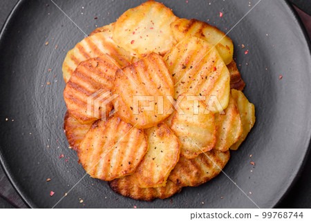 Delicious crispy fried potatoes in slices on a black ceramic plate 99768744