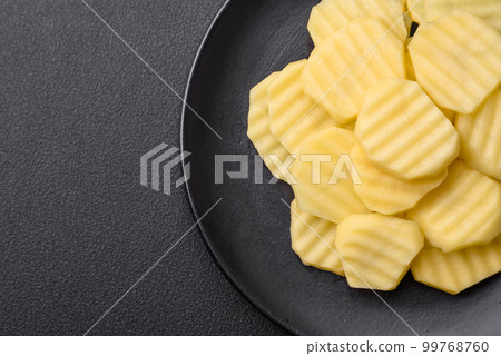 Raw fresh potatoes cut into slices on a black ceramic plate 99768760