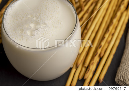 Thin and long bread sticks made of wheat flour and a glass of milk 99769347