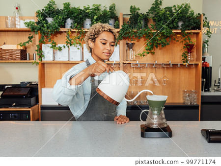 Young female barista with short hair preparing coffee with a filter at the counter 99771174