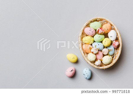 Colorful Easter eggs in wicker basket against colored background, closeup. top view with copy space 99771818