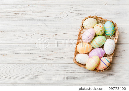 Colorful Easter eggs in wicker basket against colored background, closeup. top view with copy space 99772400
