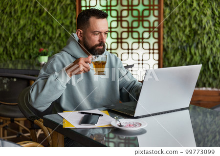 Thoughtful bearded man in casual clothes in cafe using laptop 99773099