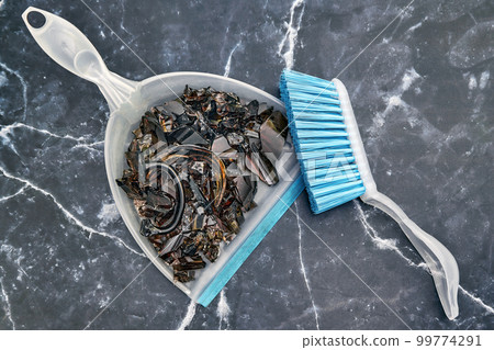 Shards of broken dark glassware on a scoop and a brush on a marble floor Shards of broken dark glassware on a scoop and a brush on a marble floor 99774291