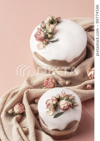Glazed Easter cakes decorated with dry tea rose flowers on pastel background. Easter composition with cakes, roses and napkin. Easter background with copy space for your design. Glazed Easter cakes decorated with dry tea rose flowers on pastel background. Easter composition with cakes, roses and napkin. Easter background with copy space for your design. 99774586