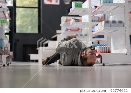 Unconscious person lying on pharmacy floor during epileptic attack, suffering from epilepsy disorder. Drugstore young client fainting, having seizure with foaming at mouth 99774621