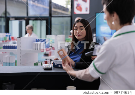 Drugstore customer waiting for cashier scanning purchase at counter desk. Young asian woman buying supplements and sunscreen, standing at pharmacy medical store at checkout Drugstore customer waiting for cashier scanning purchase at counter desk. Young asian woman buying supplements and sunscreen, standing at pharmacy medical store at checkout 99774654