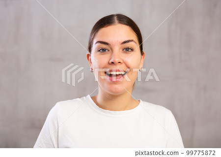 Cheery young woman posing happily against gray shadeless background 99775872