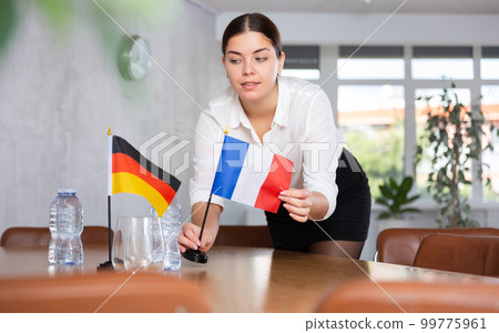 Preparing for business presentation - secretary places flags of Germany and France on negotiating table 99775961