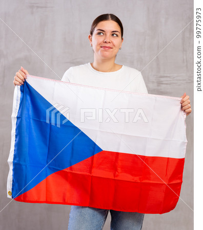 Joyous young woman holding Czech flag against unicoloured background Joyous young woman holding Czech flag against unicoloured background 99775973