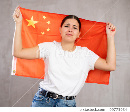 Frustrated young woman with Chinese flag against gray wall 99775984