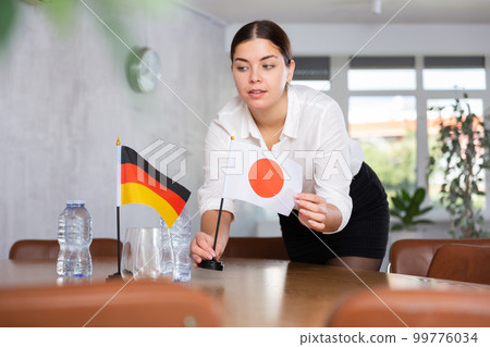 Young female attendant putting up flags for international negotiations between germany and japan Young female attendant putting up flags for international negotiations between germany and japan 99776034