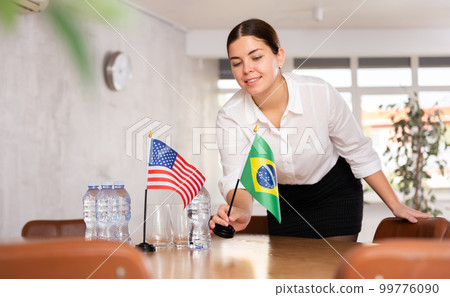 Preparing for negotiations - positive female employee of the protocol department places flags of the USA and Brazil 99776090