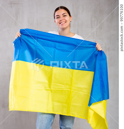 Happy girl stands with flag of Ukraine. Isolated on gray background Happy girl stands with flag of Ukraine. Isolated on gray background 99776100