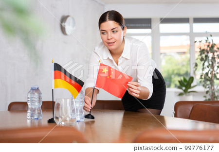 Preparing for business negotiations - woman sets small flags of countries of China and Germany on table 99776177