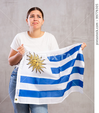 Irritated girl stands with flag of Uruguay. Isolated on gray background Irritated girl stands with flag of Uruguay. Isolated on gray background 99776305