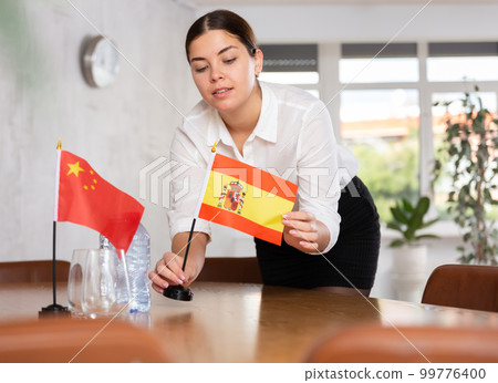 Young female attendant putting up flags for international negotiations between china and spain 99776400