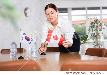 Young female attendant putting up flags for international negotiations between south korea and canada 99776539