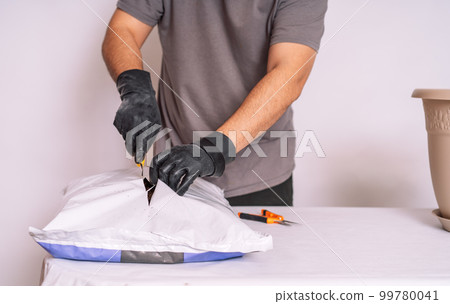 Man in black gloves cuts a bag of earth for transplanting houseplants Man in black gloves cuts a bag of earth for transplanting houseplants 99780041