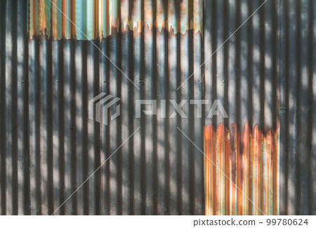 Artistic of old and rusty zinc sheet wall with The shadow of the bright sunlight shining through trees and leaves beautifully. 99780624