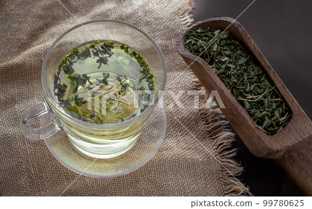Relax time with A cup of Hot Hemp Tea (CBD herbal tea) from Dried organic hemp leaves in Wooden scoop put on burlap placemat. Relax time with A cup of Hot Hemp Tea (CBD herbal tea) from Dried organic hemp leaves in Wooden scoop put on burlap placemat. 99780625