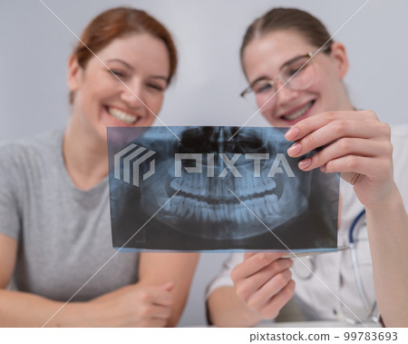 A woman doctor and a patient at the reception are discussing an x-ray of the jaw. 99783693
