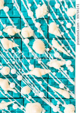 Mini mermaid chocolate bars drizzled with white chocolate, sprinkling with white pearl sugar sprinkles, and decorated with a white chocolate seashells. 99784141