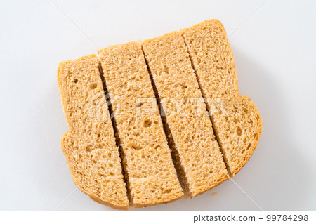 Cutting stale bread with a bread knife on a white cutting board to make croutons. Cutting stale bread with a bread knife on a white cutting board to make croutons. 99784298