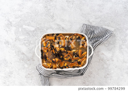 Flat lay. Cooling freshly baked bread pudding with raising and almond slivers in a white casserole dish. Flat lay. Cooling freshly baked bread pudding with raising and almond slivers in a white casserole dish. 99784299