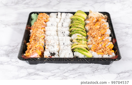 Pre-packaged variety of sushi and sushi rolls in a plastic tray. 99784537