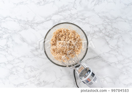 Flat lay. Shredded chicken in a pressure cooker. Shredding freshly cooked chicken breast in a glass mixing bowl with a hand mixer. Flat lay. Shredded chicken in a pressure cooker. Shredding freshly cooked chicken breast in a glass mixing bowl with a hand mixer. 99784583