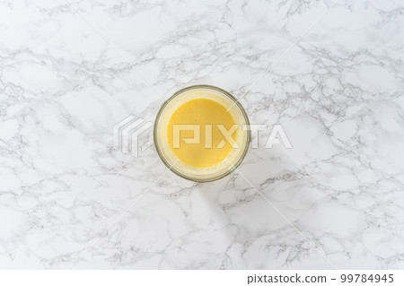 Mixing wet ingredients in a large glass mixing bowl to bake mini Easter bread kulich. Mixing wet ingredients in a large glass mixing bowl to bake mini Easter bread kulich. 99784945