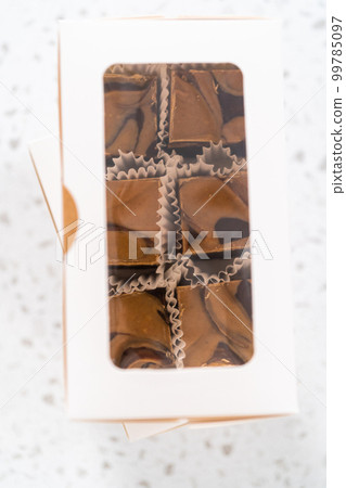 Packaging homemade chocolate fudge with peanut butter swirl into a white gift box. 99785097