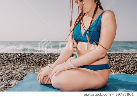 Woman sea yoga. Well looking middle aged woman with braids dreadlocks in blue swimwear doing stretching pilates on yoga mat near sea. Female fitness yoga routine concept. Healthy lifestyle. Woman sea yoga. Well looking middle aged woman with braids dreadlocks in blue swimwear doing stretching pilates on yoga mat near sea. Female fitness yoga routine concept. Healthy lifestyle. 99785961