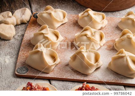 Semi finished manti dumplings on board with flour 99786042