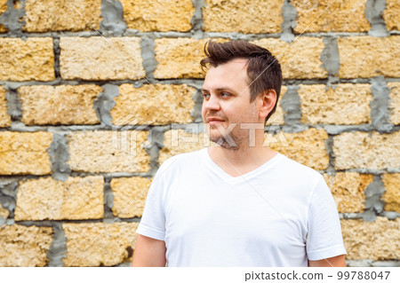 male man in white t-shirt on yellow limestone laid bricks wall background. Lifestyle looking away unshaven profile view young caucasian man portrait, close-up. Entrepreneur, businessman 99788047