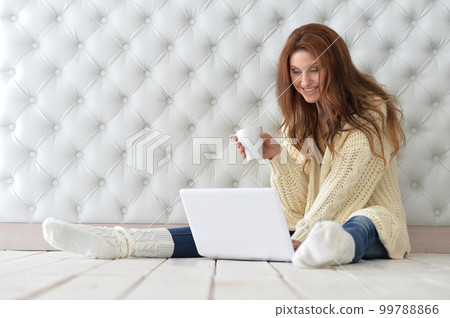 Beautiful woman with laptop sitting on floor and drinking coffee 99788866