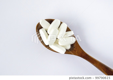 L glutamine white oval tabletsin a wooden spoon on a white background, top view. L glutamine white oval tabletsin a wooden spoon on a white background, top view. 99790615