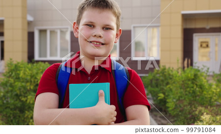 boy student with book his hand smiling. happy family. child with school backpack textbook his hands looks into frame. face child schoolboy. happy child kid teenager schoolboy school yard. education 99791084